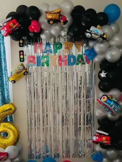 A vehicle-themed birthday decoration for a 6th birthday. The setup includes a balloon arch decorated with foil balloons of a police car, fire truck, and ambulance.