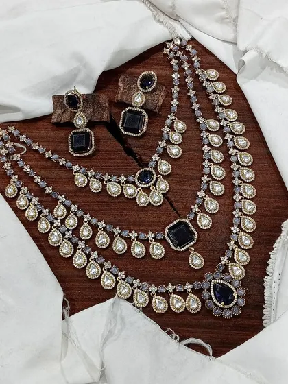 A grand, three-layered AD necklace set. This piece is designed for maximum impact, featuring square and teardrop stones, and is available in blue, green, pink, and red.