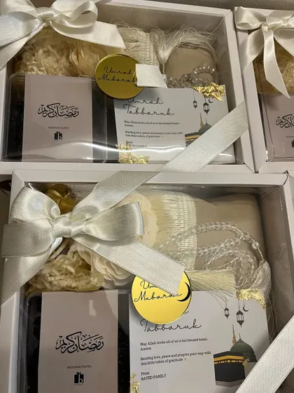 A batch of Umrah return gifts, elegantly packed in white boxes with satin ribbons and a gold "Umrah Mubarak" tag.