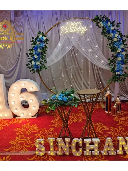 An elegant 16th birthday decoration with a floral-decorated ring backdrop, fairy lights, and large marquee numbers.