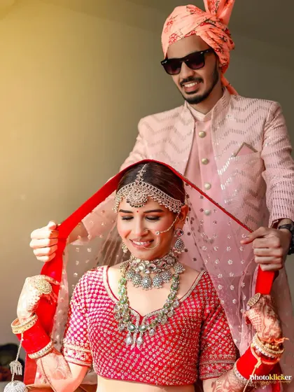 A playful and caring moment as the groom helps adjust his bride's dupatta, a candid shot that reveals their sweet relationship.