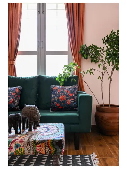 A cozy seating nook within a parent's bedroom, with a deep green velvet sofa, rust-orange curtains, and a Kantha-embroidered table.