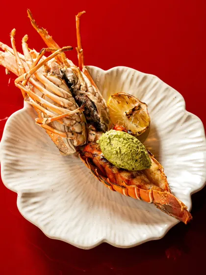 A grilled jumbo prawn with wasabi butter, presented on an elegant, shell-like plate. We focus on dramatic lighting to highlight the textures of the grilled seafood.