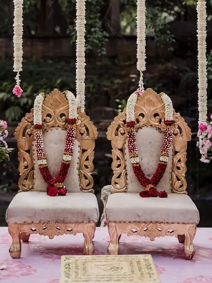Ornate golden chairs for the bride and groom at the mandap, decorated with red rose garlands.