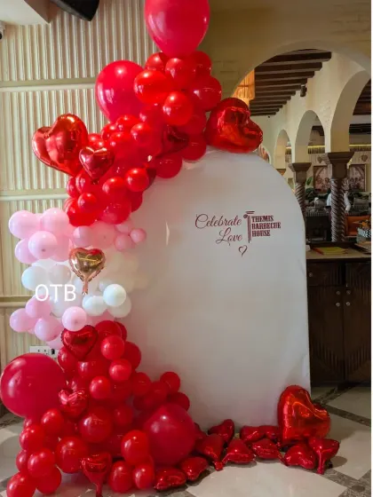 An elegant arched backdrop panel for a "Celebrate Love" theme. The panel is decorated with a cascade of red, pink, and white balloons, including shiny red heart foils.