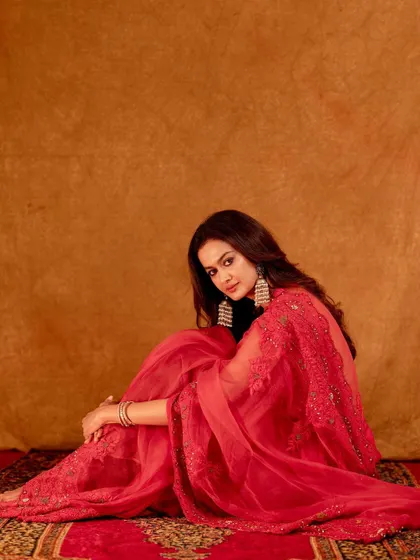 A seated portrait against a warm, earthy backdrop. This composition creates an intimate and grounded feel, drawing attention to the rich red of the traditional attire and the subject's direct, engaging gaze.