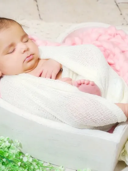 A newborn baby sleeps peacefully in a heart-shaped basket, swaddled in white. This classic pose is all about love and serenity.