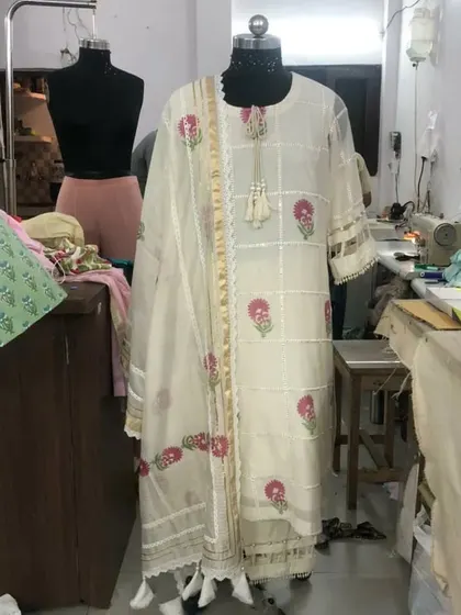 The full view of the off-white and pink floral suit on a mannequin. The design features delicate lace inserts and tassel details for a feminine touch.
