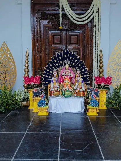 A beautiful setup for the Varapooja ceremony, with a divine idol placed against a peacock-feather-inspired backdrop and adorned with lotus flowers and traditional lamps.