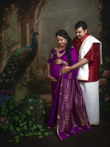 A full-length portrait of an expecting couple in a classic, artistic pose against a painted backdrop. The image has a timeless, painting-like quality, perfect for a fine art maternity session.