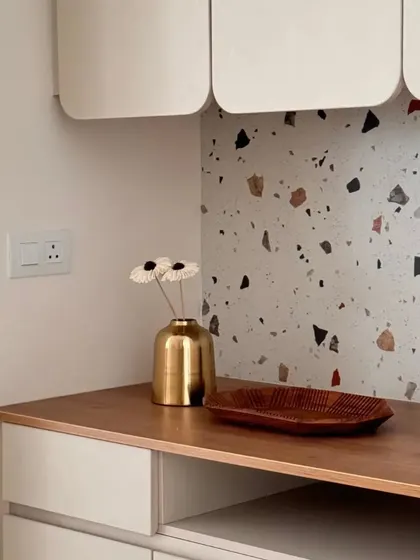 A stylishly curated corner featuring a terrazzo backsplash, a wooden countertop, and elegant overhead cabinets with curved doors.