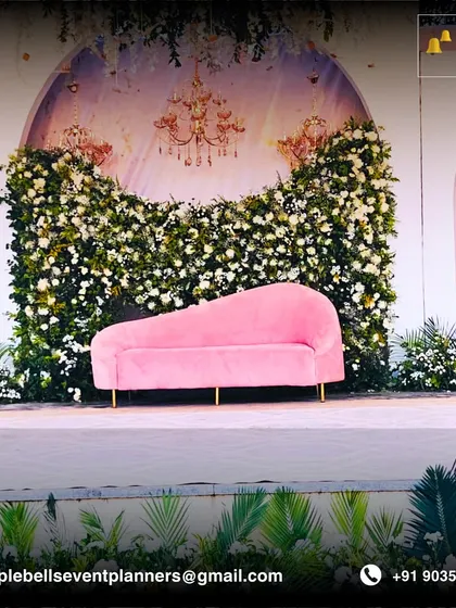 A chic and romantic stage setup perfect for an engagement or reception. A plush pink chaise lounge sits before a backdrop of white flowers and elegant chandelier illustrations, creating a soft and inviting focal point.