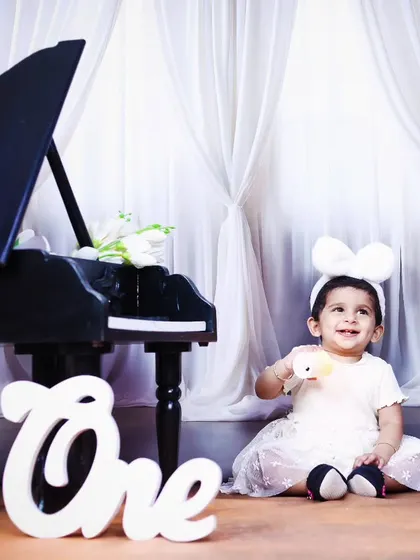 A sweet, smiling baby girl enjoying her first birthday piano-themed photoshoot.