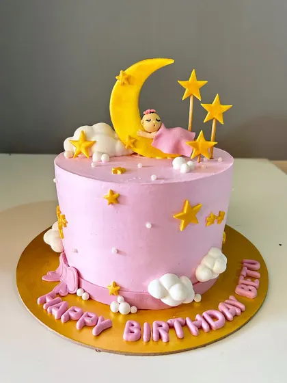 A celestial-themed first birthday cake. This dreamy pink cake features a fondant baby sleeping on a crescent moon surrounded by stars.