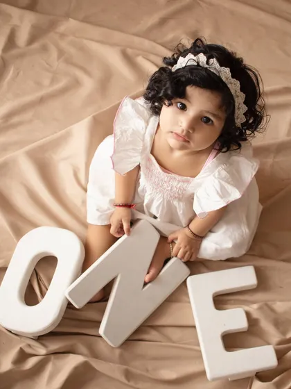 Celebrating turning one. This little girl sits with large letters spelling "ONE" for a classic first birthday photo.