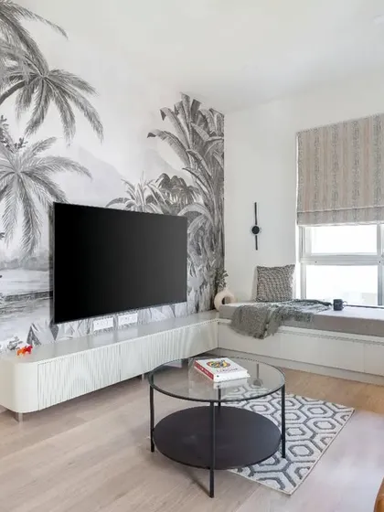 A modern living room with a tropical twist. A large, monochromatic palm-themed mural serves as a stunning feature wall, complemented by a sleek white TV unit and a cozy window seat.