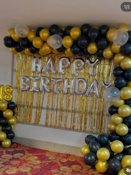 An 18th birthday setup with a gold shimmer curtain and a black and gold balloon arch.