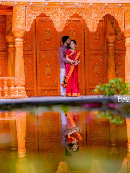 A tender moment captured against a vibrant orange backdrop. The reflection in the water adds a beautiful symmetry to this portrait of a couple in traditional Indian outfits.