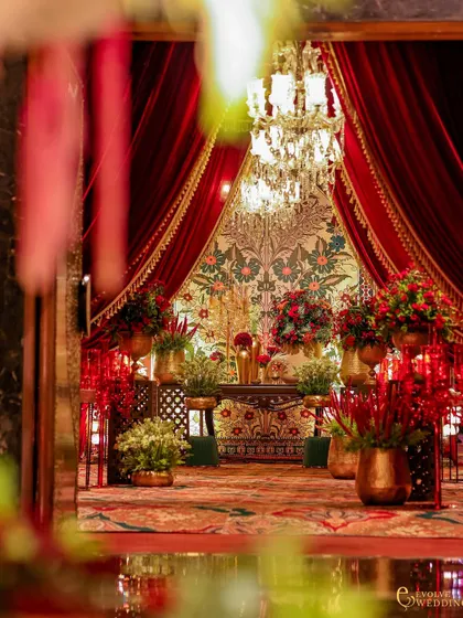 A glimpse into a lavishly decorated space through an archway, framed by rich red velvet curtains. A crystal chandelier and a detailed tapestry backdrop add layers of regal opulence.