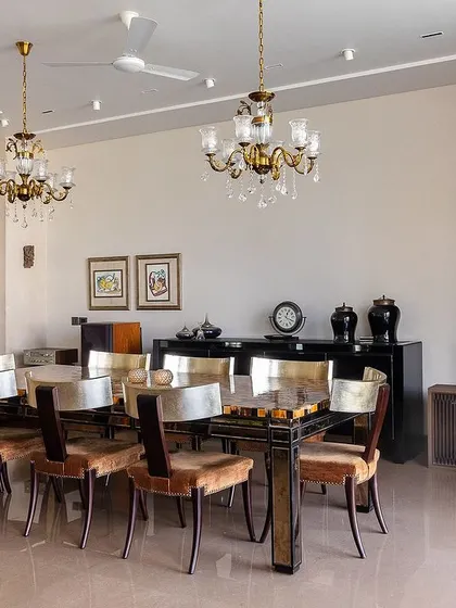 The dining area in The Brick House features a unique tabletop with a patchwork of wood and metal, paired with classic chandeliers. This space was designed to accommodate the client's existing collection while maintaining a cohesive feel.