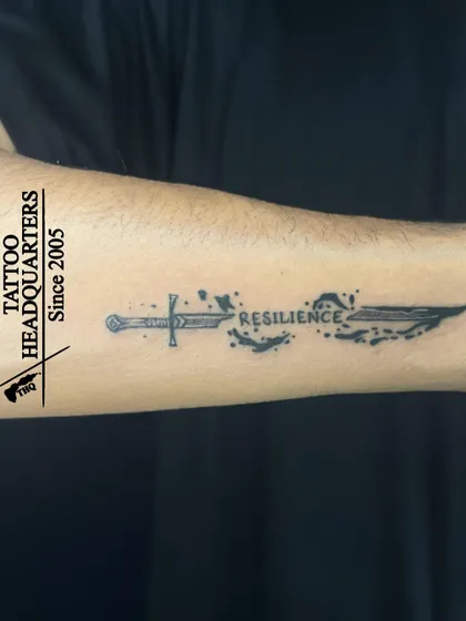 A creative tattoo of a sword transforming into the word "RESILIENCE," symbolizing strength and overcoming adversity.