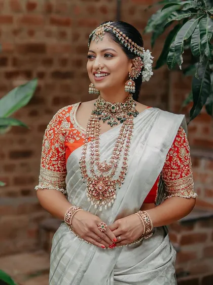 A full-length shot of the bride, her white and red Kanjeevaram creating a stunning contrast with the lush green background.