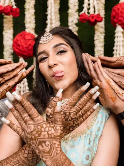 Fun and candid moments from a mehendi ceremony. The bride's makeup is fresh and playful, with a winged liner and glowing skin, perfect for celebrating with her loved ones. The hairstyle is a soft half-updo with pretty accessories.