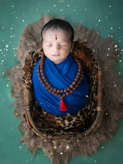 A serene and divine portrait for Mahashivratri. This newborn is styled as a tiny devotee of Lord Shiva, complete with a rudraksha necklace and a blue wrap.