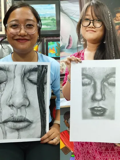 Two students proudly displaying their hyper-realistic pencil portraits. Our advanced classes focus on capturing emotion and fine details like water droplets and hair texture.