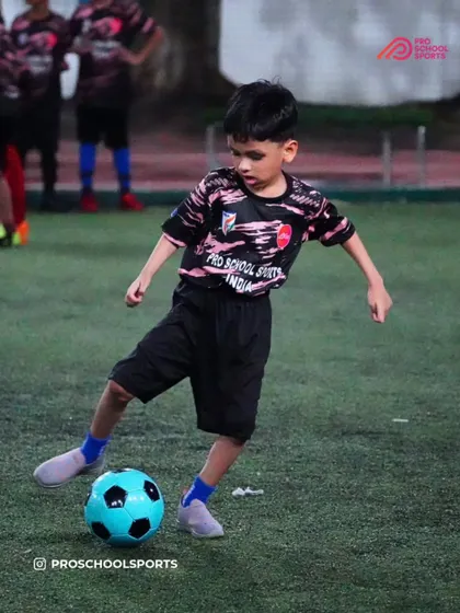 A young player dribbles with a bright blue ball, fully engaged in the training drill.
