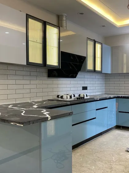 Another view of the stylish blue modular kitchen, highlighting the L-shaped layout and the beautiful contrast between the blue cabinets, black countertop, and white tiles.