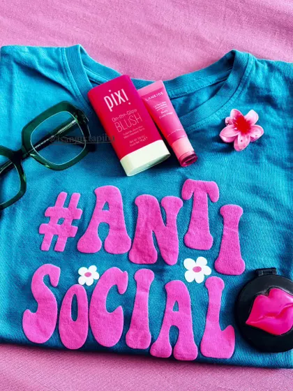 A fun, themed flatlay with a quirky 'Anti-Social' t-shirt and matching pink beauty products. This shows my playful side and ability to create content around a specific mood or phrase.