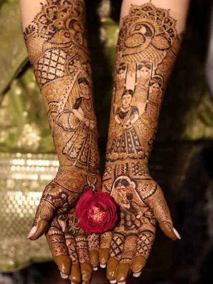 A beautiful shot of a completed bridal mehndi, held with a single red rose. The design features portraits and intricate patterns, symbolizing love and beauty.
