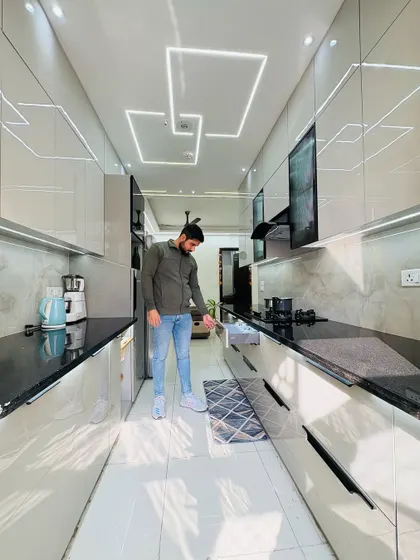 A full view of a sleek parallel kitchen with glossy light grey cabinets and a black countertop. The design includes profile lighting on the ceiling and under the cabinets, ensuring a well-lit and modern cooking space.