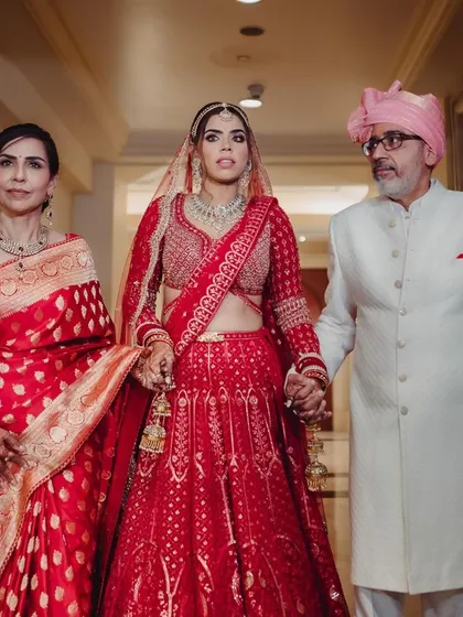 A poignant moment as the bride walks with her parents. Dressed in a classic red lehenga, she holds her father's hand, capturing the emotion and significance of the transition.