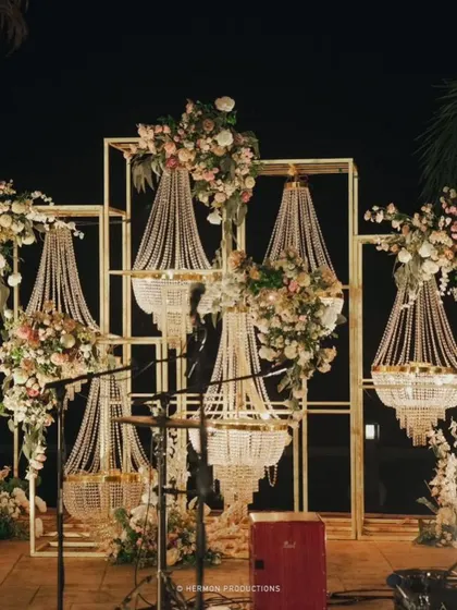 A stunning backdrop for the engagement stage, featuring geometric gold frames, hanging pearl chandeliers, and fresh florals.