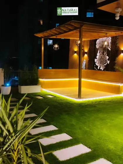 A wooden pergola with built-in seating at our Gwal Pahari project, beautifully lit against the night sky.