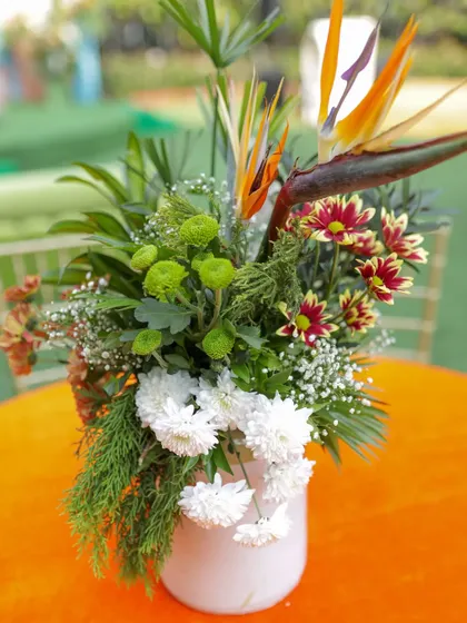 A vibrant centerpiece for a Haldi lunch, featuring Birds of Paradise, chrysanthemums, and other colorful flowers in a simple white vase.