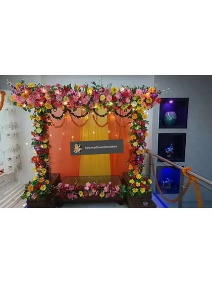 This is a simple stage-style decoration for a home Ganpati celebration. I used a backdrop of orange and yellow drapes with a floral border and fairy lights to create a warm and inviting space for pooja.