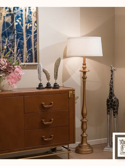 This elegantly crafted floor lamp features a gold-finished turned wood base and a simple white shade. It provides beautiful ambient light and stands as a classic, sculptural element in the room.