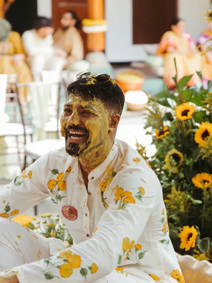 The groom enjoying his Haldi ceremony, his face covered in turmeric paste as he laughs heartily. This image captures the fun and playful side of the ritual.