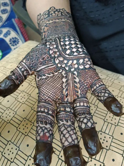 A close-up of a freshly applied henna design with filled fingertips. The dark paste promises a rich, deep stain once it's removed.