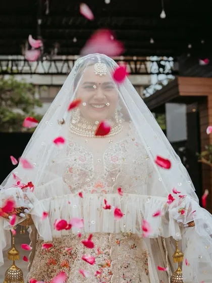 A beautiful bridal entry shot, with the bride smiling through her veil as rose petals shower down on her. A moment of pure joy and celebration.
