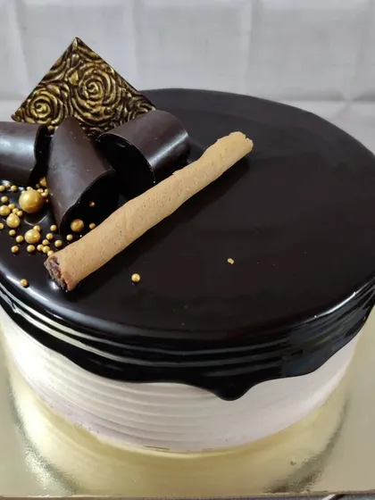 A sophisticated chocolate drip cake. It's decorated with dark chocolate curls, a wafer roll, and a touch of gold for a luxurious finish.
