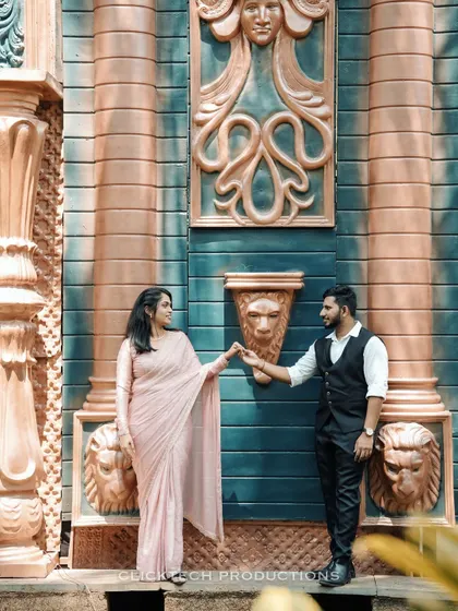A creative pose against a wall with Greco-Roman-style carvings, the couple in traditional outfits, creating a unique fusion look.