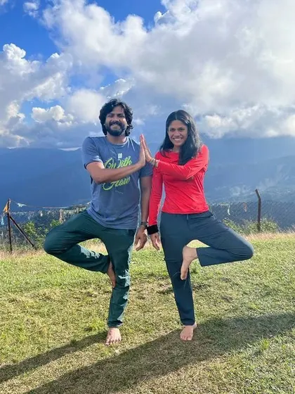 Two practitioners finding their balance together in Vrikshasana amidst the green hills of Nepal.