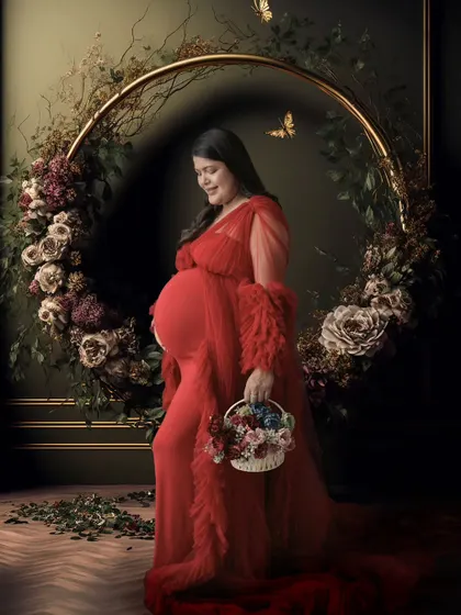A dark and moody floral-themed portrait. The mom-to-be stands in a red gown before a large floral wreath, with digital butterflies added for a touch of whimsy.