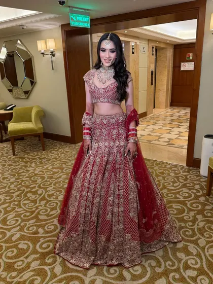 A full-length shot showing the grandeur of her red bridal lehenga. The makeup and open hairstyle with a maang tikka create a look that is both traditional and effortlessly modern.