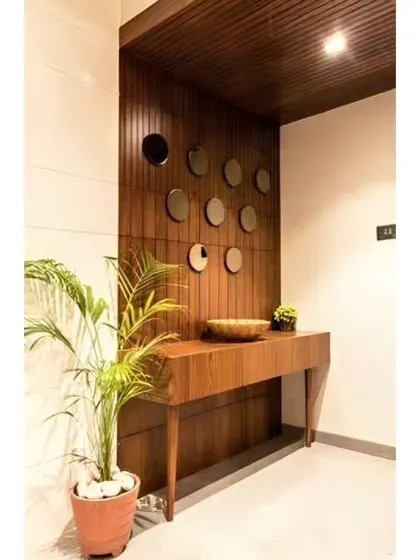 A minimalist foyer with a simple wooden console table against a fluted wood accent wall. The small decorative mirrors and potted plant add a touch of nature.