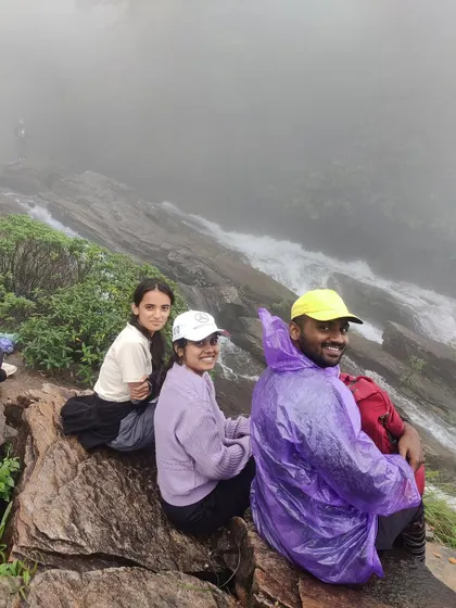 Three friends sitting at the top of Bandaje Falls, enjoying the misty view.